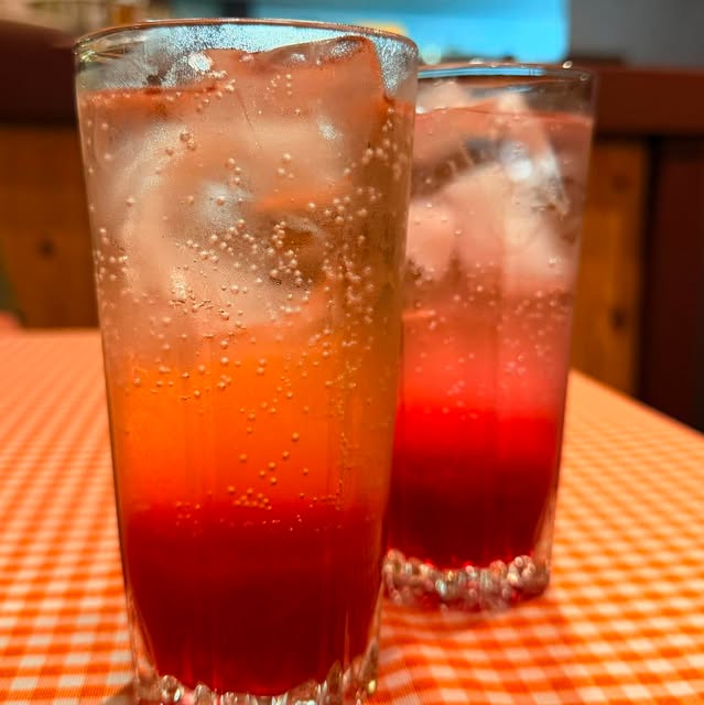 Dois copos de limonada rosa gelada em degradê de laranja e vermelho