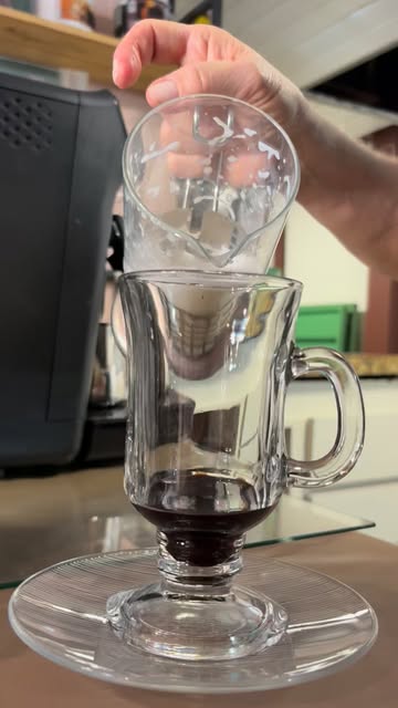Mão despejando de uma jarra de vidro em um copo de vidro com café escuro no fundo
